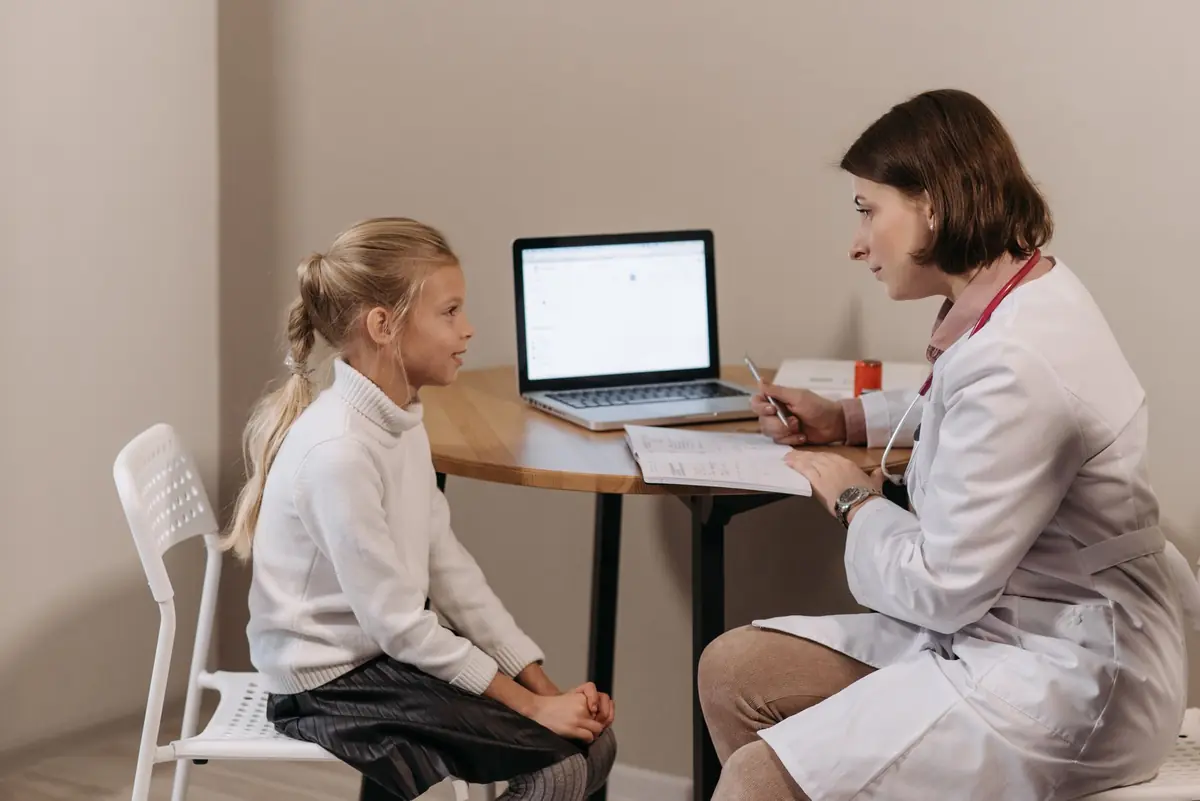 A clinician at a desk speaking with a child and using a laptop during an appointment