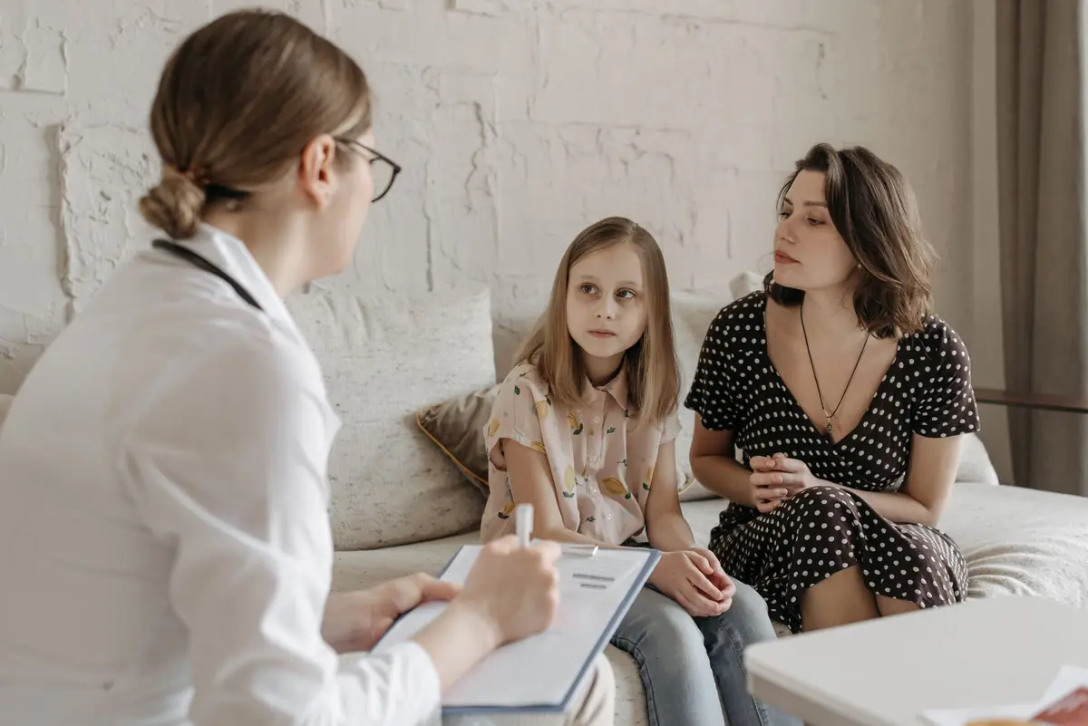 A clinician taking notes while talking with two seated patients in a calm consulting room