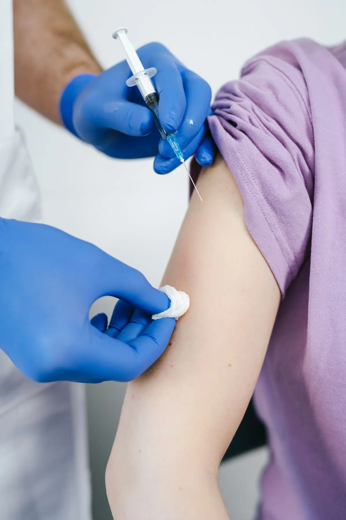 A gloved clinician giving a vaccination into a patient's upper arm