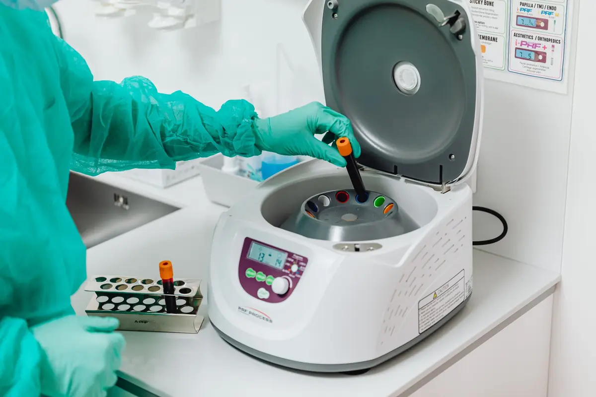 A laboratory worker in protective clothing loading samples into a bench centrifuge